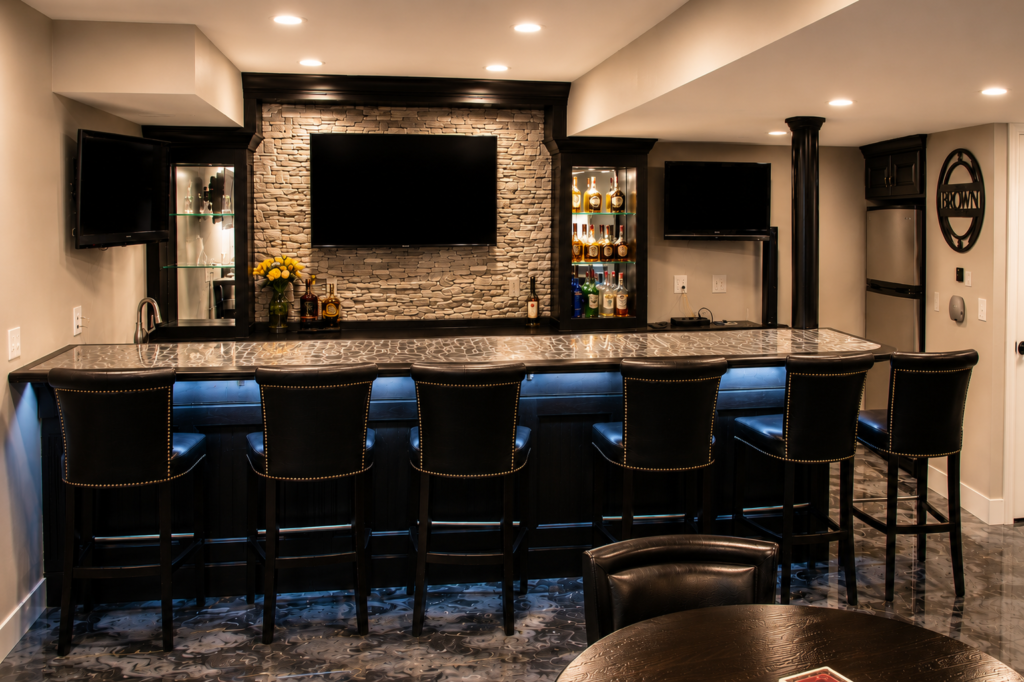 Custom black entertainment bar with epoxy metallic laminate countertop, integrated downlighting, wet bar, illuminated display cabinets and seating.